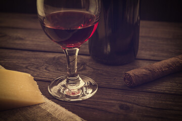 Bottle of red wine with a glass of red wine and a piece of parmesan and cuban cigar on an old...