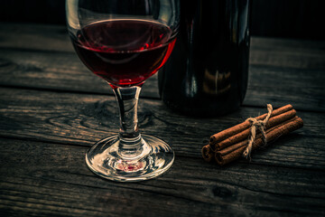 Bottle of red wine with a glass of red wine and  cinnamon sticks tied with jute rope on an old wooden table. Angle view, focus on the glass of red wine