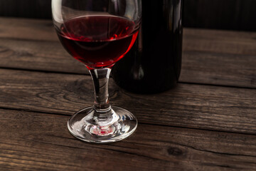 Bottle of red wine with a glass of red wine on an old wooden table. Angle view, focus on the glass of red wine
