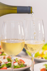 Pouring white wine next to assortment of salads: Selective focus. Healthy food and lifestyle concept.