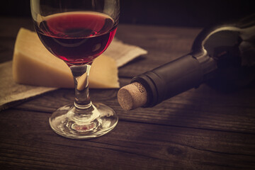 Bottle of red wine with a glass and a piece of parmesan on an old wooden table. Angle view