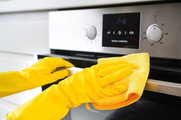 Cleaning service or housework. Female hand in a yellow rubber glove wipes built-in oven in a...