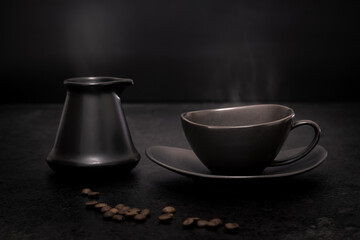 Obraz na płótnie Canvas Low key still-life of a black coffee cup on a saucer and a black Turkish coffee pot with traces of steam above against a black background