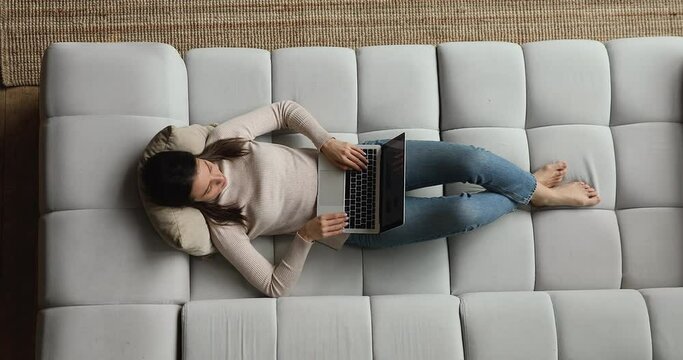 Young woman relax on sofa with laptop top overhead view. Female spend weekend use internet wi-fi connection and modern wireless computer, chat in social media, search information, websurfing concept