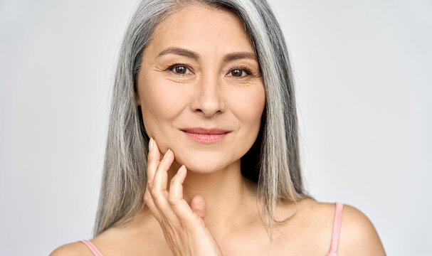 Closeup portrait of gorgeous happy middle aged mature asian woman, senior older 50 year lady looking at camera touching her face isolated on white. Ads of lifting anti wrinkle skin care treatment.