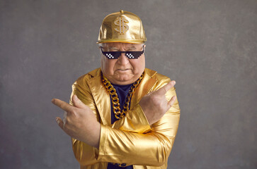 Retired older adult man in thug life glasses, gold chain and disco outfit isolated on gray...