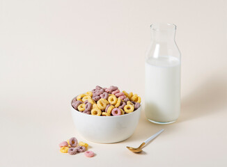 sweet colorful cornflakes rings in a white bowl with spoon and a bottle of milk on a yellow background. Front view and copy space