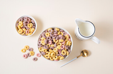sweet colorful cornflakes rings in a white bowl with spoon and a jug of milk on a yellow background. Top view and copy space