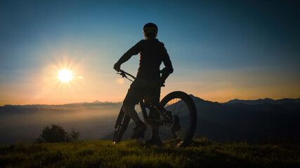Silhouette of a woman on mountain bike looking at sunset