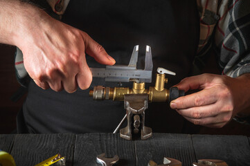 The wizard measures the size of fitting using a caliper before connecting water or gas pipe. Closeup of the hands of the master plumber in workshop