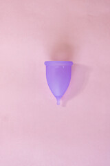 purple menstrual cup on a plain pink background