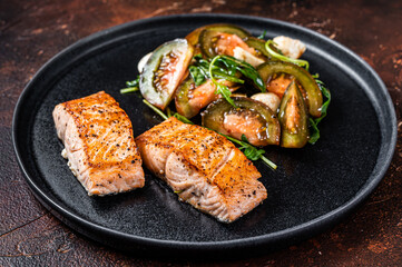 Grilled Salmon Fillet Steaks with arugula and tomato salad on a plate. Dark background. Top view