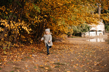 Fototapeta premium Goldener Herbst, ein 4-jähriges Mädchen in einem grauen Mantel läuft in der Nähe des Sees im Herbstpark