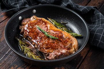 Grilled new york strip beef meat steak in a pan with herbs. Dark wooden background. Top view