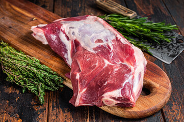 Raw lamb or goat shoulder meat on the bone on a wooden butcher cutting board with cleaver. Dark...