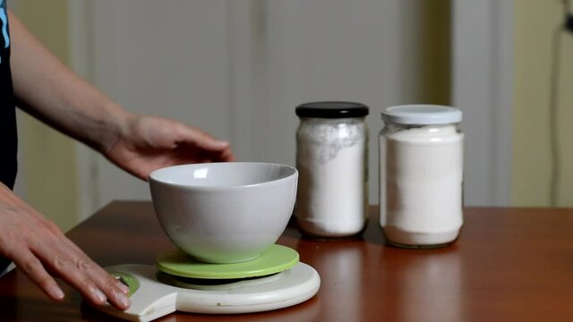 A woman chooses a jar of powdered sugar and weighs it on a kitchen scale