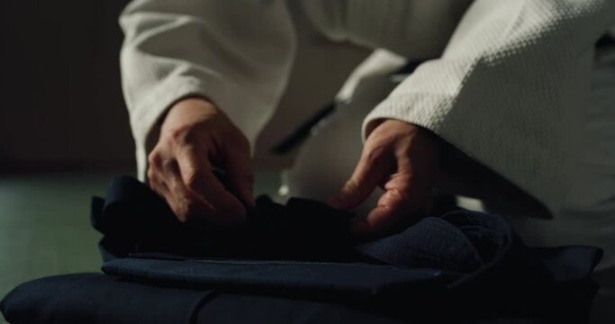Cinematic macro of mature female fighter folding her hakama before practicing Aikido in martial arts school. Concept: healthy lifestyle, sports, recreation, defense, religious beliefs