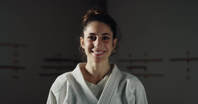 Cinematic shot of young female budokai fighter is smiling in camera after practicing Aikido in Japanese martial arts school. Concept: healthy lifestyle, sports, recreation, defense, religious beliefs