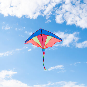 Colorful bright rainbow kite hovering in the blue sky with white clouds