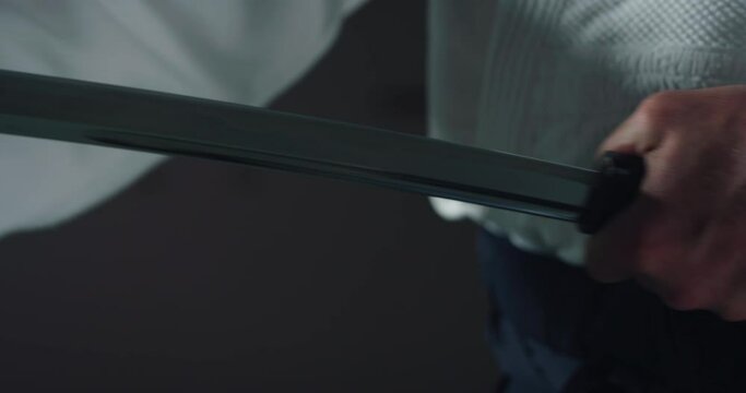 Cinematic macro of fighter master is pulling out katana sword before Aikido training in modern Japanese martial arts school. Concept of sports and recreation, philosophy, defense, religious beliefs.