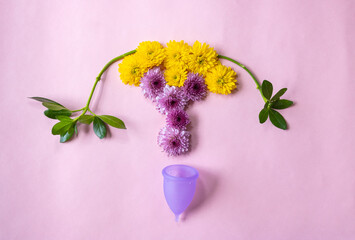 Purple menstrual cup with flowers simulating the figure of a uterus, on a plain pink background.