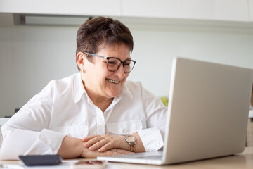 Smiling mature middle aged business woman using laptop working on computer,distance learning from...