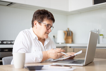 mature middle aged business woman using laptop working on computer with documents, sitting at desk. 