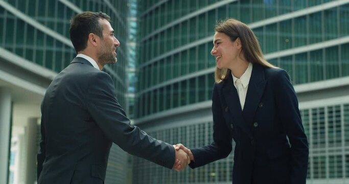 Cinematic shot of smiling business partners in formal apparel are shaking hands before to start meeting on skyscrapers background. Concept of corporate, finance, deal, success, cooperation, teamwork.