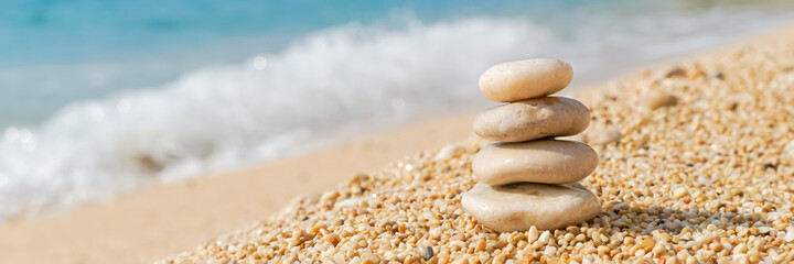 Fototapeta na wymiar Pyramid stones balance on the sand of the beach. Zen balance, minimalism, harmony and peace. Wide banner, selective focus