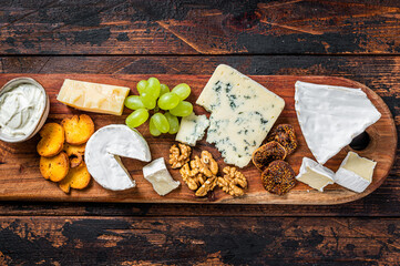 Assorted Cheese board with Brie, Camembert, Roquefort, parmesan, blue cream cheese, grape and nuts. Dark wooden background. Top view