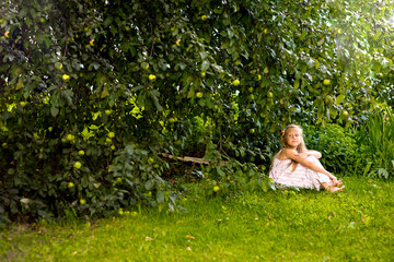 Naklejka na ściany i meble Blonde girl and toddler in light clothes sitting under an apple tree with green apples outdoors, healthy eating, healthy childhood, selective focus