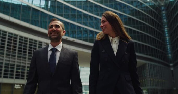Cinematic shot of happy smiling business colleagues in formal apparel are walking satisfied with their work after leaving the offices. Concept of corporate, company, success, cooperation, teamwork.