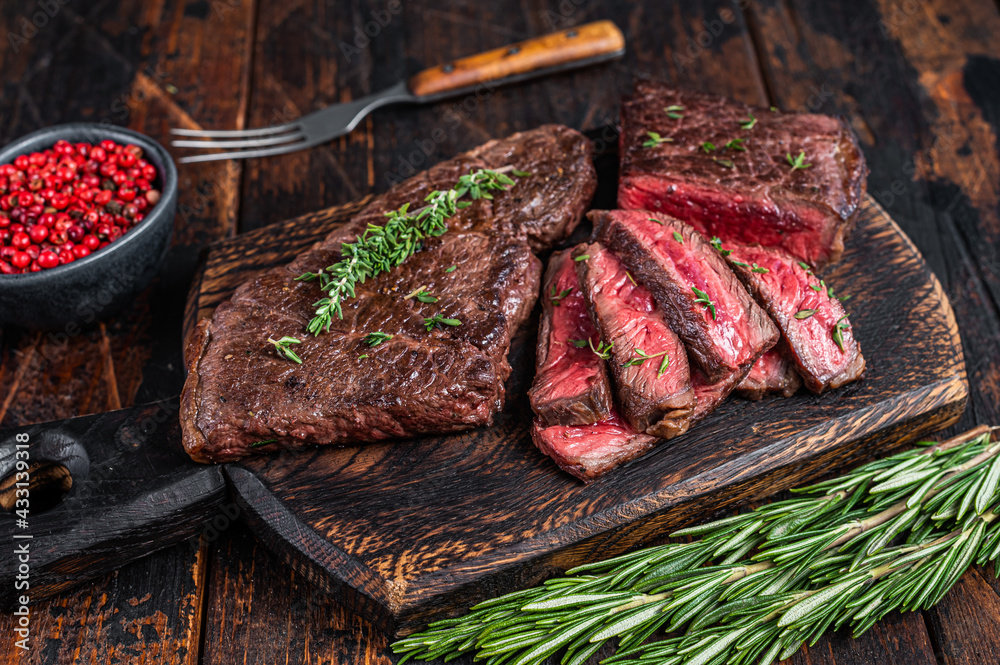 Wall mural Grilled sliced skirt beef meat steak on a cutting board with herbs. Dark wooden background. Top view