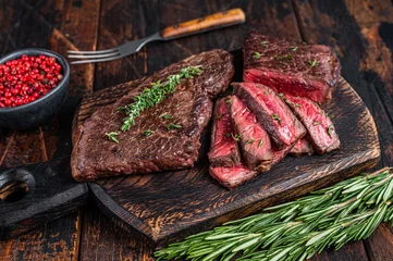Poster Grilled sliced skirt beef meat steak on a cutting board with herbs. Dark wooden background. Top view © Vladimir