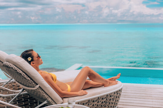 Luxury vacation in paradise Bora Bora high end resort hotel bikini woman relaxing lying on lounger sunbathing by the swimming pool at overwater villa suite.