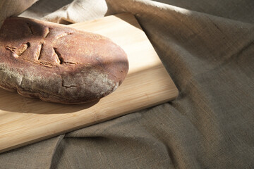 Freshly baked brown rye bread lies on a bamboo board on a canvas cloth in the falling natural light...