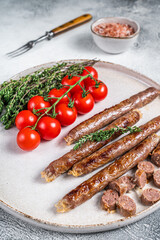 Grilled lamb meat sausage on a plate with herbs and tomato. White background. Top view