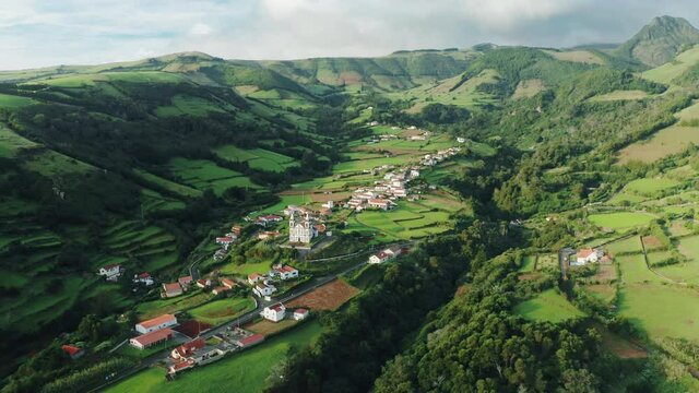 Drone shot of Fazenda De Santa Cruz town in valley, Flores Island, Azores, Portugal, Europe. Panoramic view of village houses surrounded green mountains and fields, 4k footage 