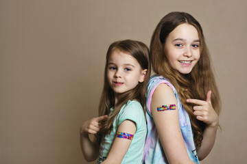 Two girls vaccinated against coronavirus infection smile and point a finger at the vaccination site