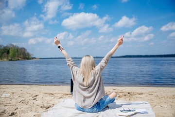 Rear view of female freelancer in blonde hair and with raised arms celebrating success.