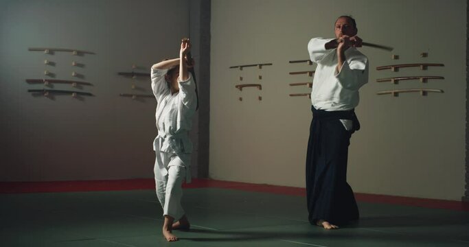 Cinematic shot of budokai fighter master and his pupil practicing with wooden sword Aikido training in modern Japanese martial arts school. Concept of sports, recreation, defense, religious beliefs.