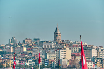 Fototapeta premium Turkey istanbul. Famous galata tower of istanbul taken photo from istanbul bosphorus and eminonu with many turkish flag during rainy day and overcast sky.