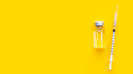 Bottle of vaccine and syringe on yellow background with copy space.