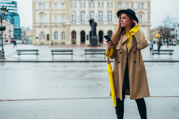 Woman using smartphone and holding a yellow umbrella outside