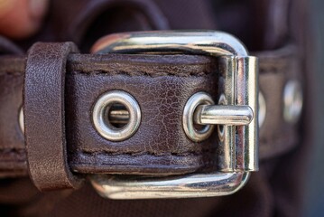 one metal white buckle on a brown leather harness bag strap