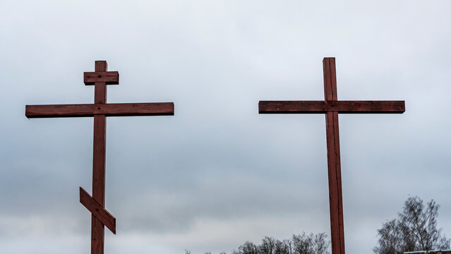Orthodox and Catholic crosses side by side on dramatic sky background. The concept of unity of faith. Space for text.