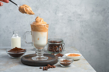 A woman's hand puts foam in dolgano coffee on a gray background.