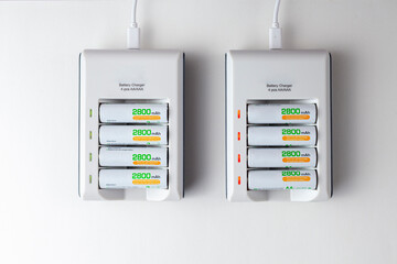 flat lay image of two rechargeable battery chargers powered through USB cables. Each has a stack of 4 AA rechargeable batteries with 2800 mAh capacity. Green and red light indicates charge levels.