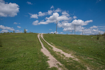 Obraz premium Landscape with an empty dirt road through a field under a blue sky with clouds.