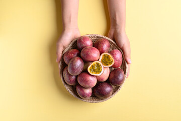 Fresh passion fruit in a basket holding by woman hand on yellow background